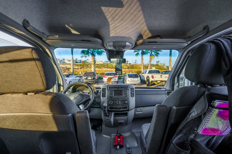 Inside this RV rental's cockpit, the dashboard and seats are visible, looking out to a sunny parking lot with palm trees. A power inverter is on the floor. — photo 8