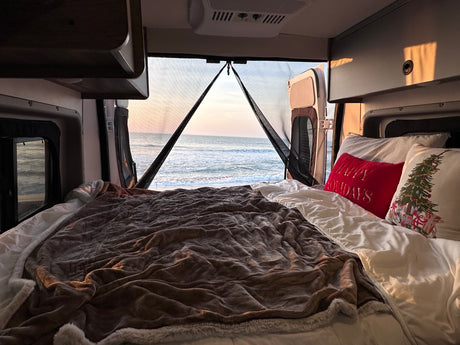 Wake up to a stunning ocean view in this cozy RV rental bed, featuring holiday pillows. Ideal for beachside campervan travel.