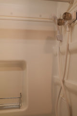 Clean RV rental shower interior with a handheld shower, clear knob faucet, and built-in shelving.