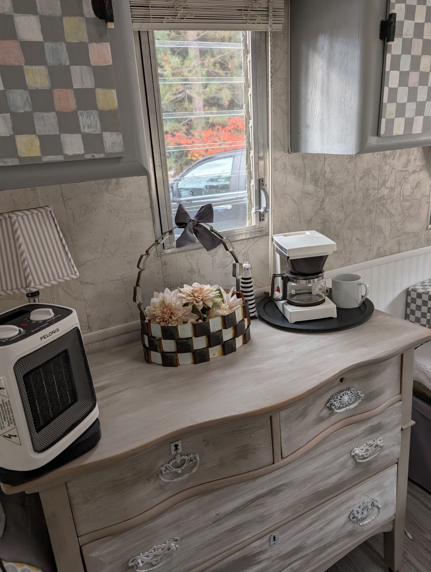 Cozy RV rental interior: dresser with heater, coffee maker, and floral decor near window.