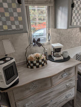 Cozy RV rental interior: dresser with heater, coffee maker, and floral decor near window.
