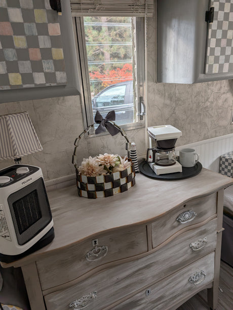 Cozy RV rental interior: dresser with heater, coffee maker, and floral decor near window.