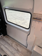 Spacious RV rental interior showing a large window looking onto gravel, light wood-look flooring, and clean white paneling.