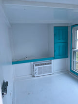 Interior view of a cozy white RV rental, showing a Midea AC, turquoise cabinets, and window.