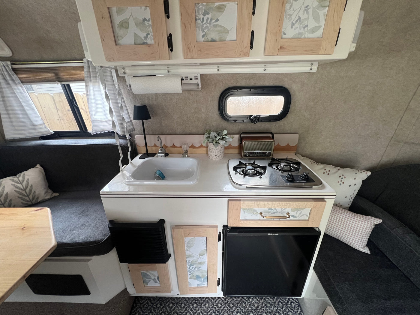 This rv rental features a compact kitchenette with a sink, two-burner stove, small fridge, and comfy bench seating. — photo 5