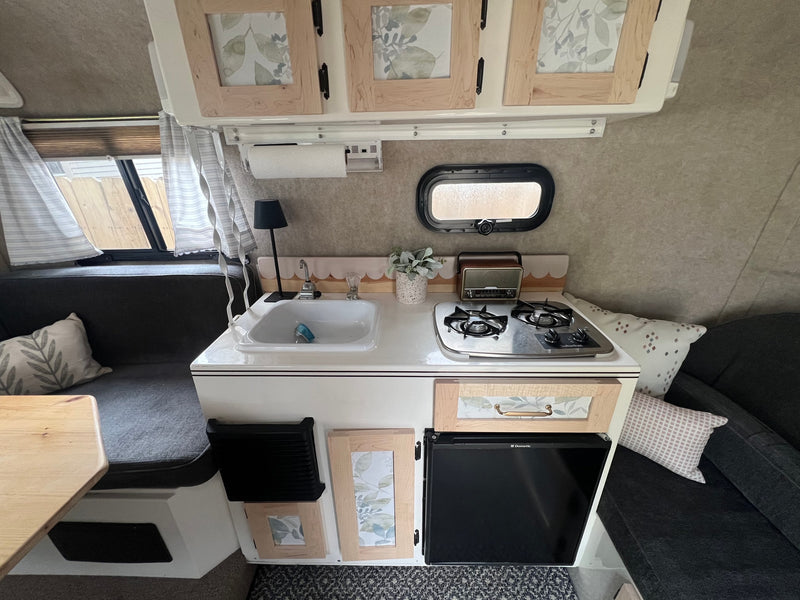 This rv rental features a compact kitchenette with a sink, two-burner stove, small fridge, and comfy bench seating. — photo 5