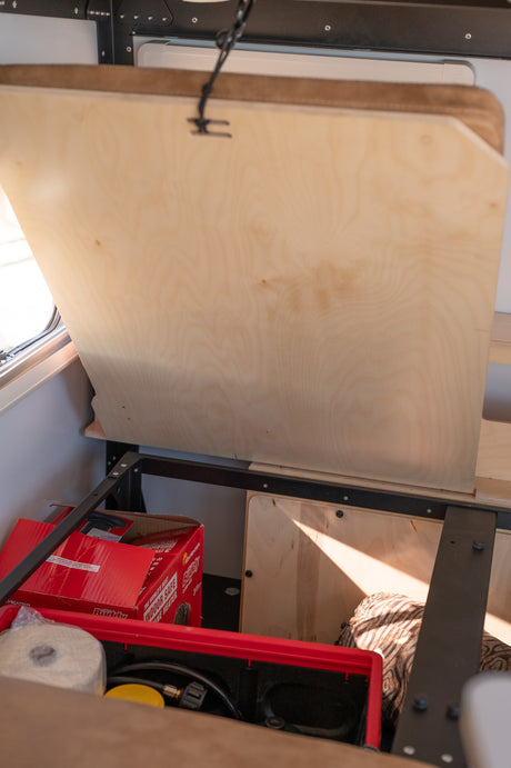 RV rental: Lifted wooden panel reveals organized under-bed storage with a "Little Buddy" heater and utility items.