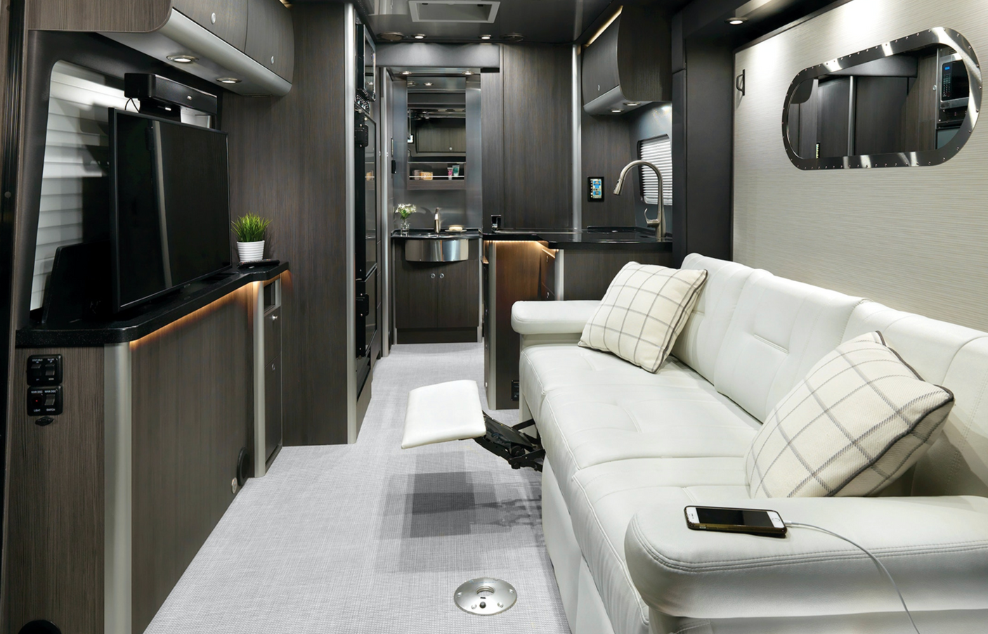 Inside a sleek **RV rental**: modern kitchen, white leather sofa, and TV create a luxurious travel experience.