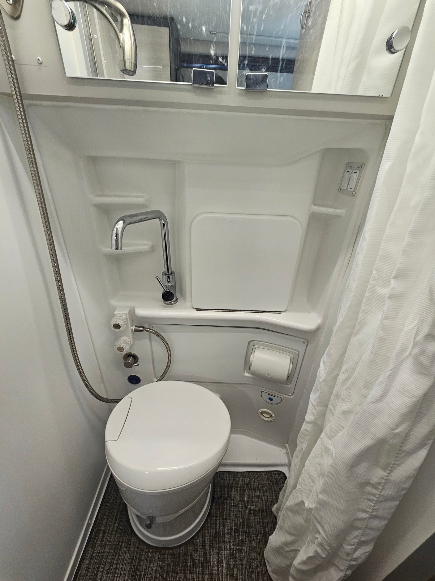 An RV rental's compact wet bath, showcasing the toilet, shower head, sink faucet, and mirror.