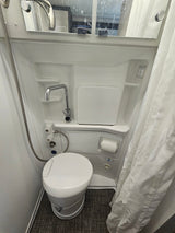 An RV rental's compact wet bath, showcasing the toilet, shower head, sink faucet, and mirror.