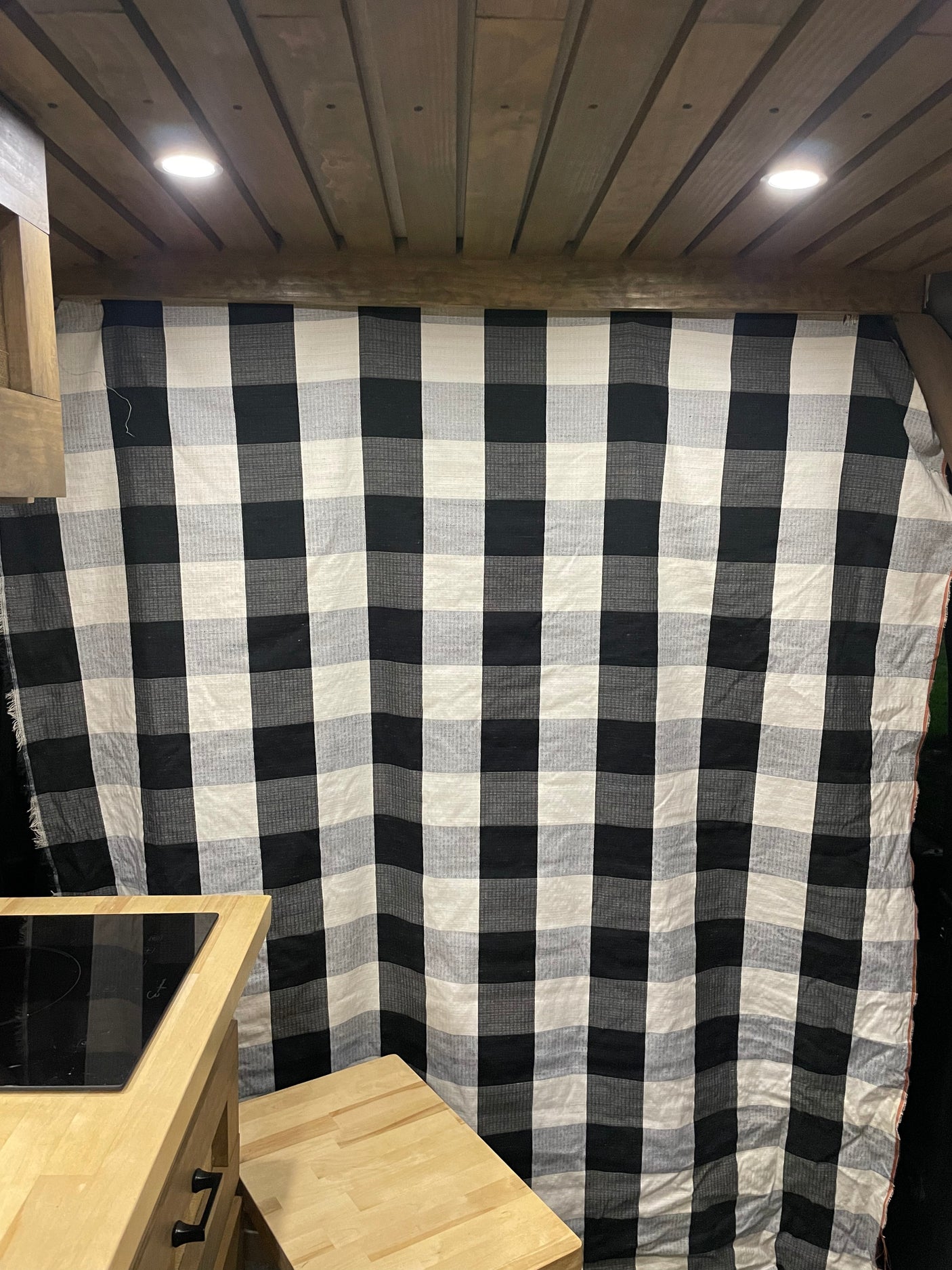 RV rental interior featuring a wood plank ceiling, checkered curtain, and kitchenette with cooktop.