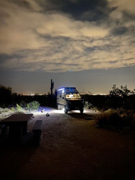 Nighttime desert view with a cozy **RV rental** parked under illuminated clouds & city lights.