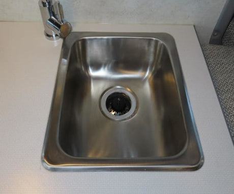 This rv rental features a compact stainless steel sink and chrome faucet on a white countertop, ready for use.