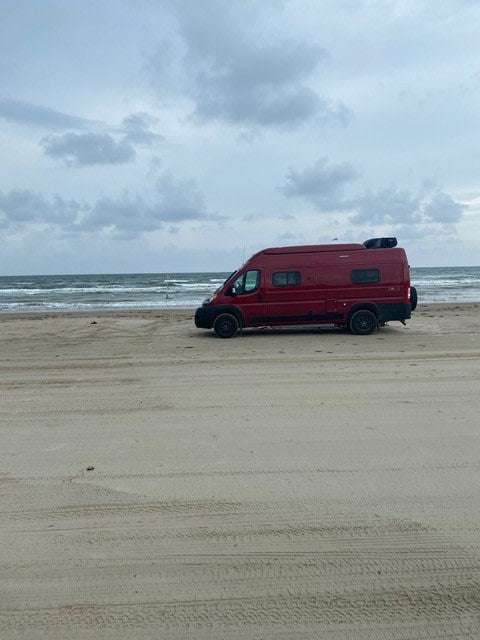 Red rv rental parked on a vast sandy beach with ocean waves under a cloudy sky, ready for adventure travel. — photo 5