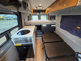 Spacious rv rental van interior with a kitchenette, convertible seating/beds, a large rear bed, and overhead storage.