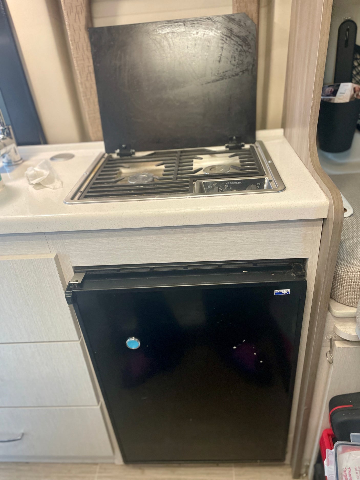 Compact RV rental kitchen with a Dometic cooktop, sink, and Norcold mini-fridge below the counter.
