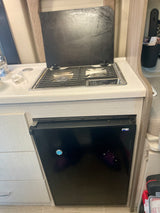 Compact RV rental kitchen with a Dometic cooktop, sink, and Norcold mini-fridge below the counter.