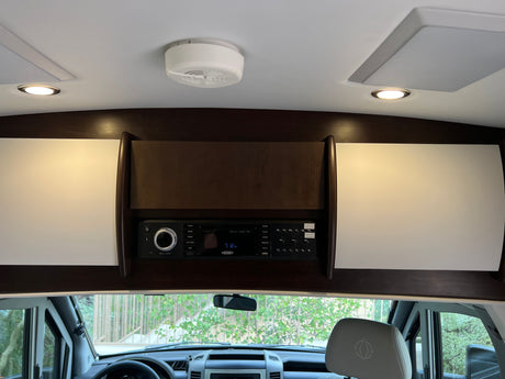 Overhead panel in an RV rental with a Jensen stereo, ceiling lights, and storage, viewed from the driver's seat.