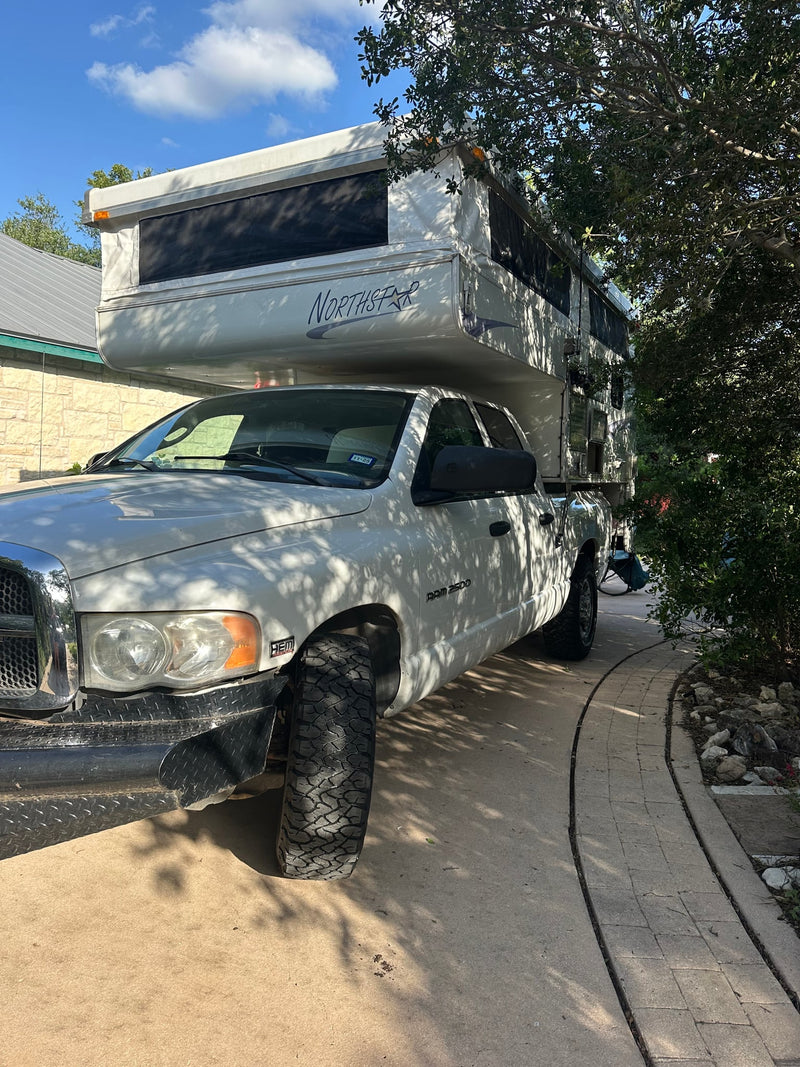  surrounded by towering pines.|A white Dodge Ram 2500 pickup truck with a Northstar pop-up RV camper — photo 2