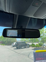 Inside a vehicle: rearview mirror with backup camera. Outside, a parking lot with vehicles, incl. a 'FOR SALE' SUV. Great for rv rental ideas.