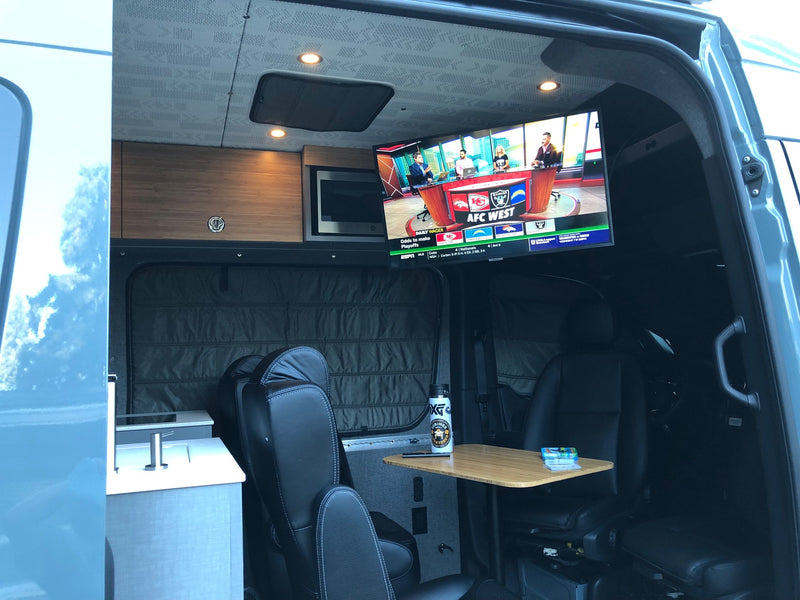 Spacious RV rental interior with a TV displaying AFC West football, kitchenette, and comfortable seating. Perfect for road trips! — photo 4