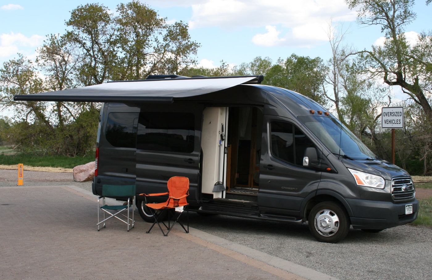 A modern grey Ford Transit camper van with an extended awning and open door, ideal for an RV rental adventure. — photo 2