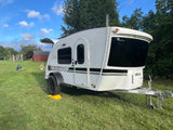 Compact white teardrop **rv rental** on green grass, parked under a blue sky. Ready for your next outdoor camping trip.