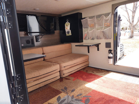 Inside an RV rental: a versatile living space with foldable couches, wall-mounted TV, organized storage, and a folding table.