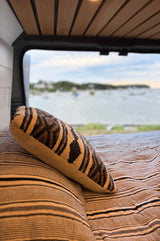 Cozy RV rental bed with a patterned pillow and a view of a tranquil bay with anchored boats.