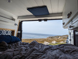 Cozy RV rental interior with bed and open doors revealing stunning ocean view. Perfect for van life adventures.