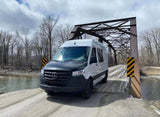 White Sprinter van RV rental on a rustic wooden bridge over a river with bare trees. Ready for adventure!