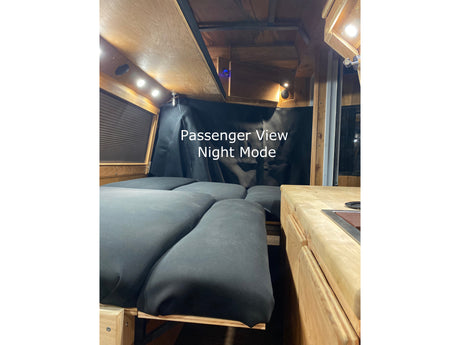 Passenger view of a cozy RV rental interior at night: a comfy bed, wooden walls, & compact kitchen.