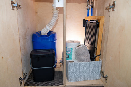 RV rental: Organized under-sink cabinet with blue water tank, drain, compost bin, and cooking essentials for a convenient trip.