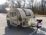 Compact RV rental: a light teardrop camper in a parking lot, ready for your next camping or outdoor adventure.