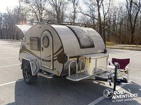 Compact RV rental: a light teardrop camper in a parking lot, ready for your next camping or outdoor adventure.