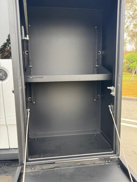 Open black storage cabinet in an RV rental, showing a shelf and bottom compartment, ideal for organized adventure gear.
