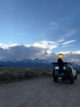 Person in a truck camper overlooking snow-capped Grand Teton mountains & vast plains. Perfect RV rental for an overland adventure!
