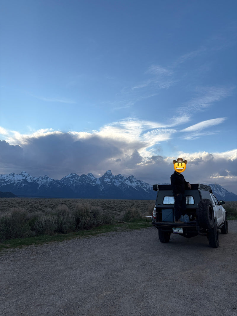 Person in a truck camper overlooking snow-capped Grand Teton mountains & vast plains. Perfect RV rental for an overland adventure! — photo 8