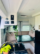 Inside a modern RV rental: a bright living area with a dinette, kitchen boasting marble-patterned counters, and accessible control panel.