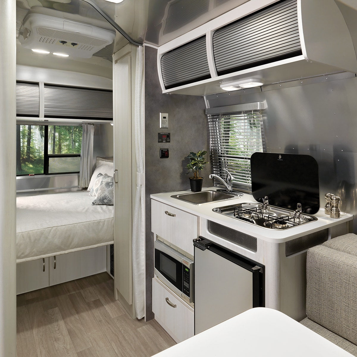RV rental interior: a bright space featuring a compact, well-equipped kitchen and a cozy bedroom with window views of a forest. — photo 7