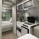 RV rental interior: a bright space featuring a compact, well-equipped kitchen and a cozy bedroom with window views of a forest.