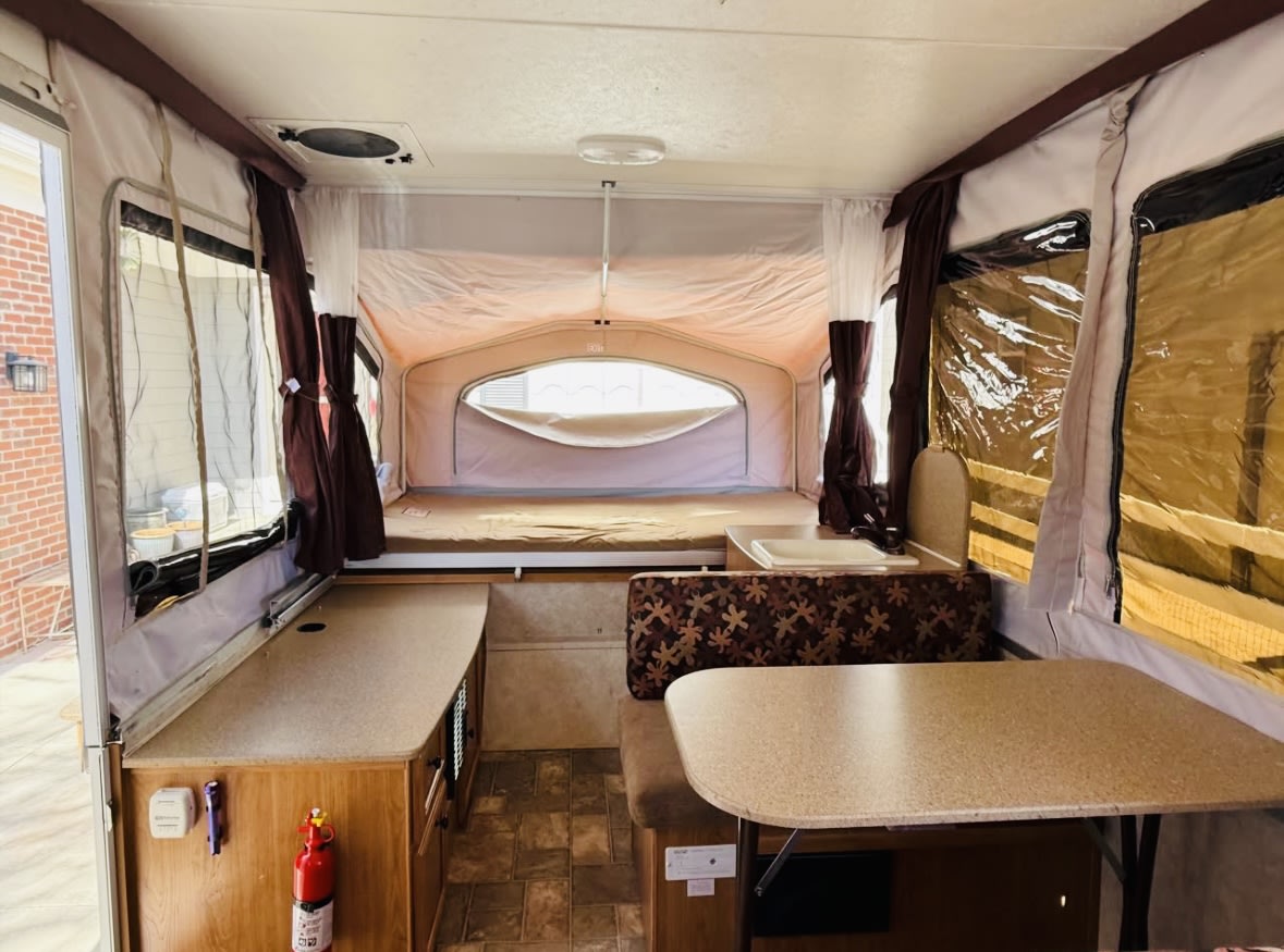 Spacious RV rental pop-up camper interior with beds, dinette, sink, and ample counter space for travel. — photo 3