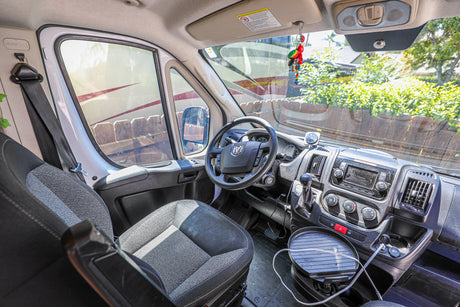 Inside a spacious RV rental van, featuring the driver's seat, dashboard, and steering wheel. Views of another RV outside.