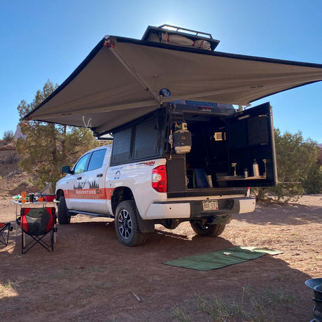 Overland adventure awaits! White truck camper with awning & full setup, an ideal RV rental for off-grid camping.
