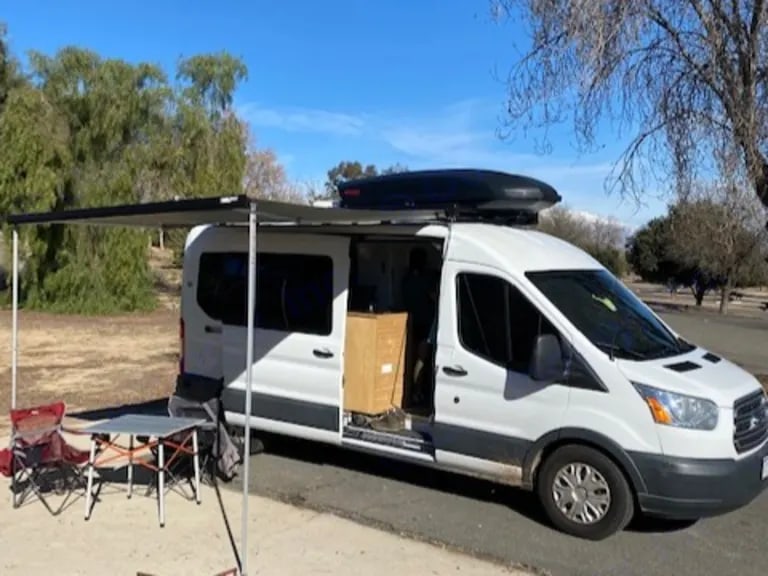 This RV rental, a white camper van, is set up with an extended awning, table, and chairs for outdoor use. — photo 17