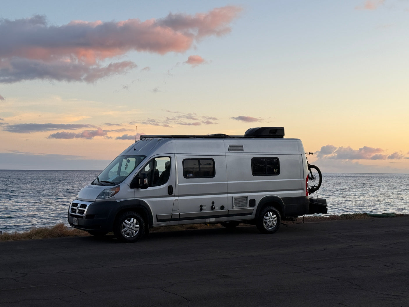 Experience van life! This RV rental camper van is parked by the serene ocean at sunset with a bike.