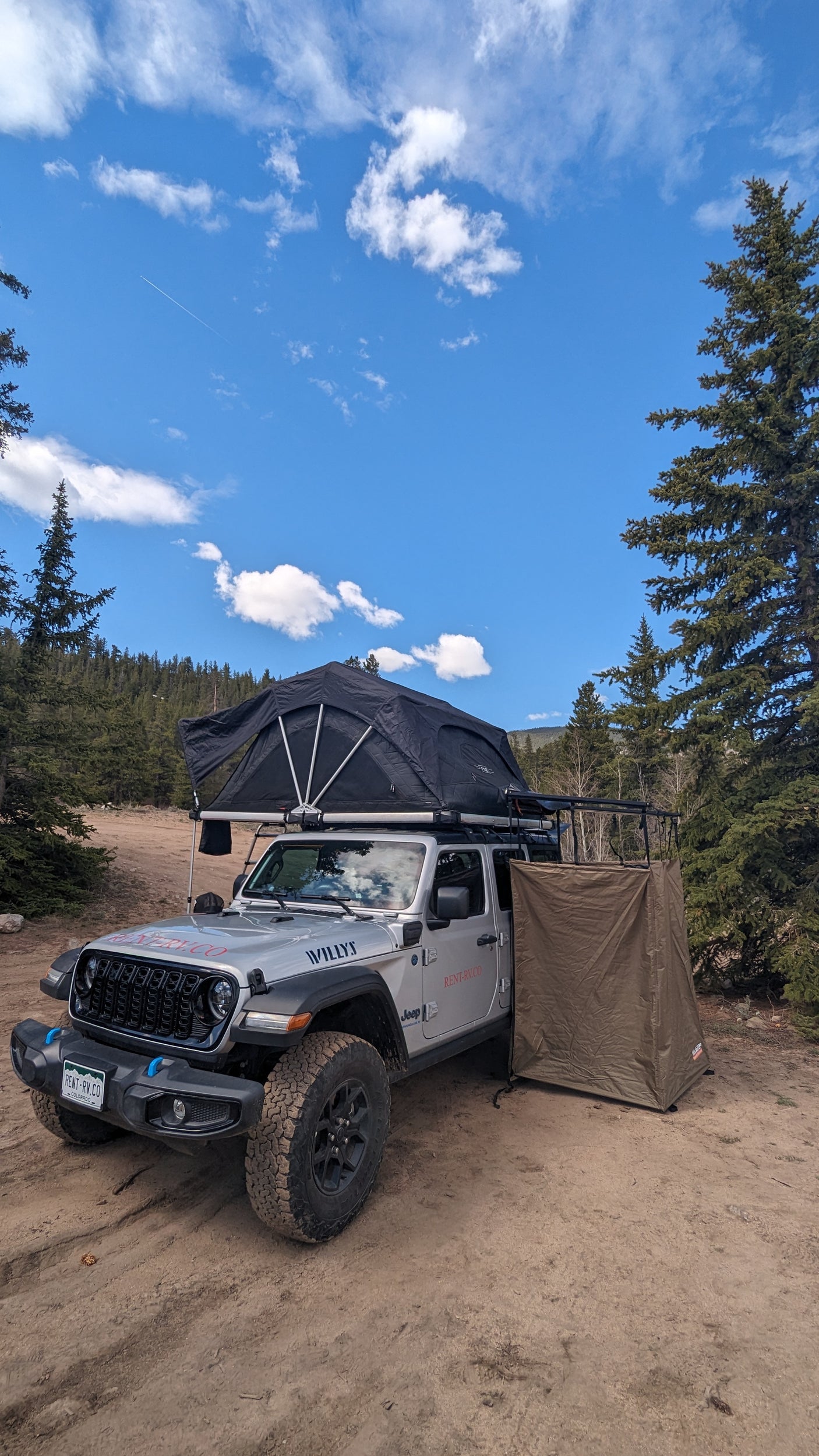 RV rental Jeep with rooftop tent & privacy shelter for off-road camping adventures under a blue sky.