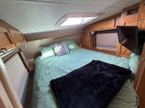 Cozy RV rental bedroom with a comfy bed, green bedding, skylight, and wooden accents, perfect for your next adventure.
