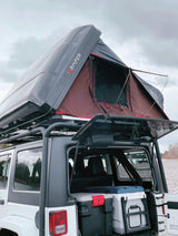 An RV rental showing a Jeep with a deployed iKAMPER rooftop tent, packed with coolers for overlanding by the lake.