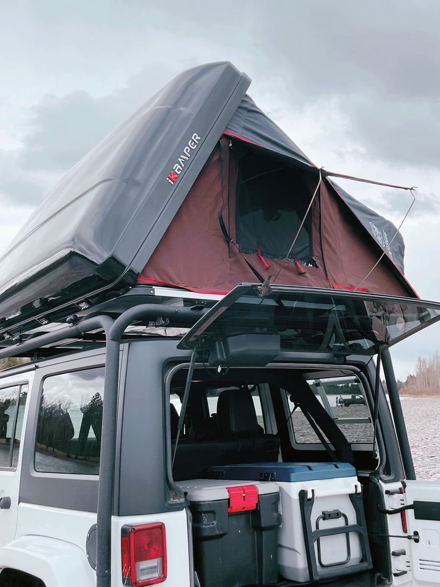 An RV rental showing a Jeep with a deployed iKAMPER rooftop tent, packed with coolers for overlanding by the lake.
